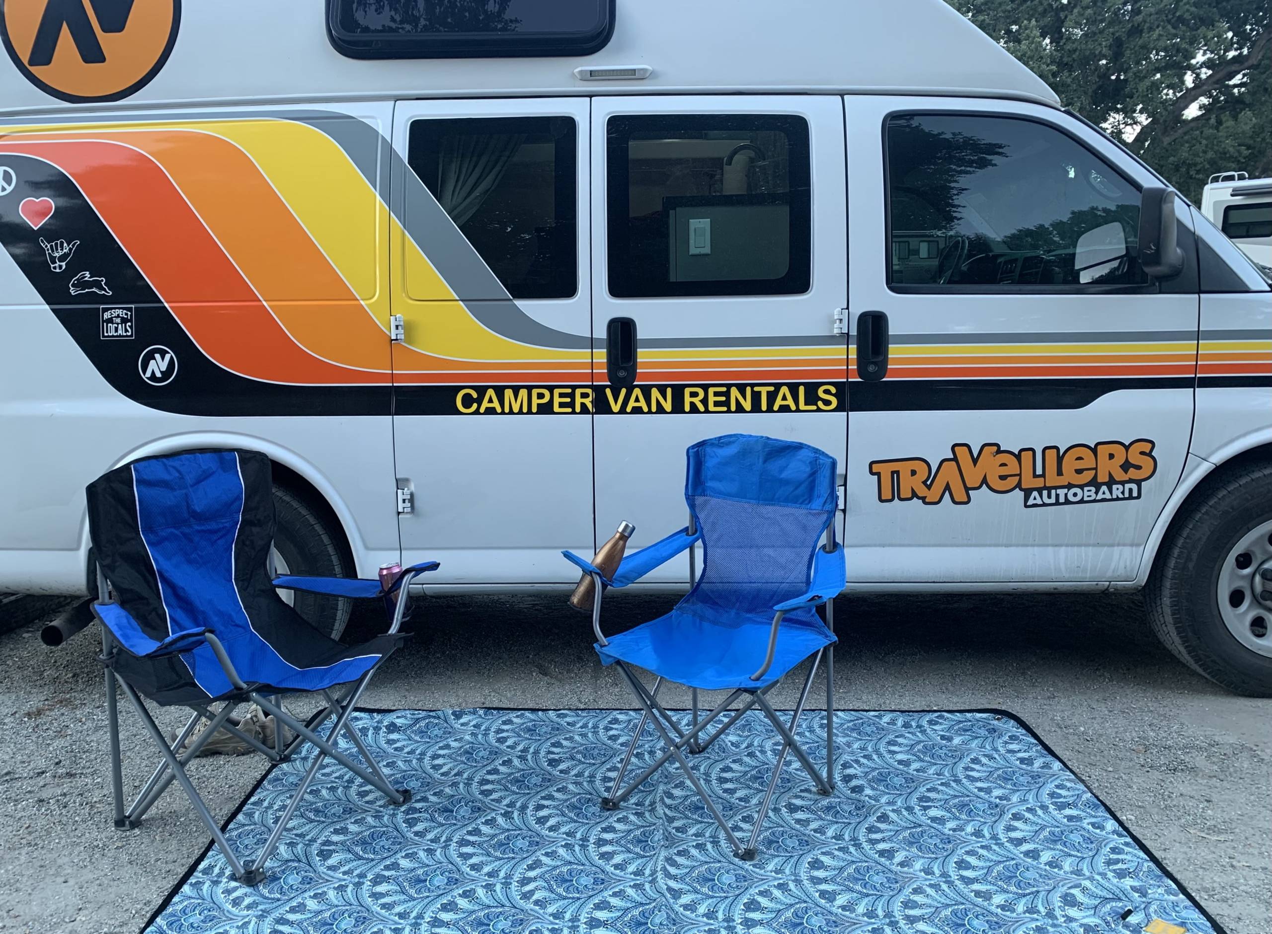 Travellers Autobarn campervan at camp with camp chairs and a blanket outdoors